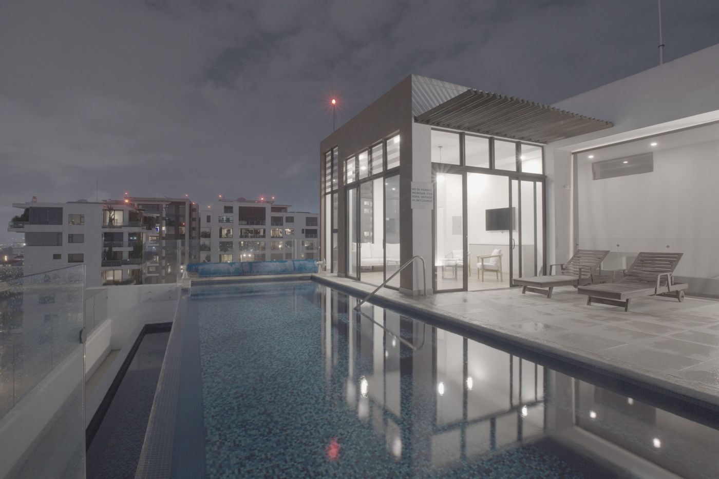 Flat unedited image: Rooftop pool at night with the city behind it